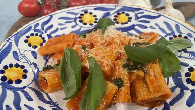 Pasta med tomatsås, riven ost och basilika på en vit tallrik målad med blåa och gula mönster